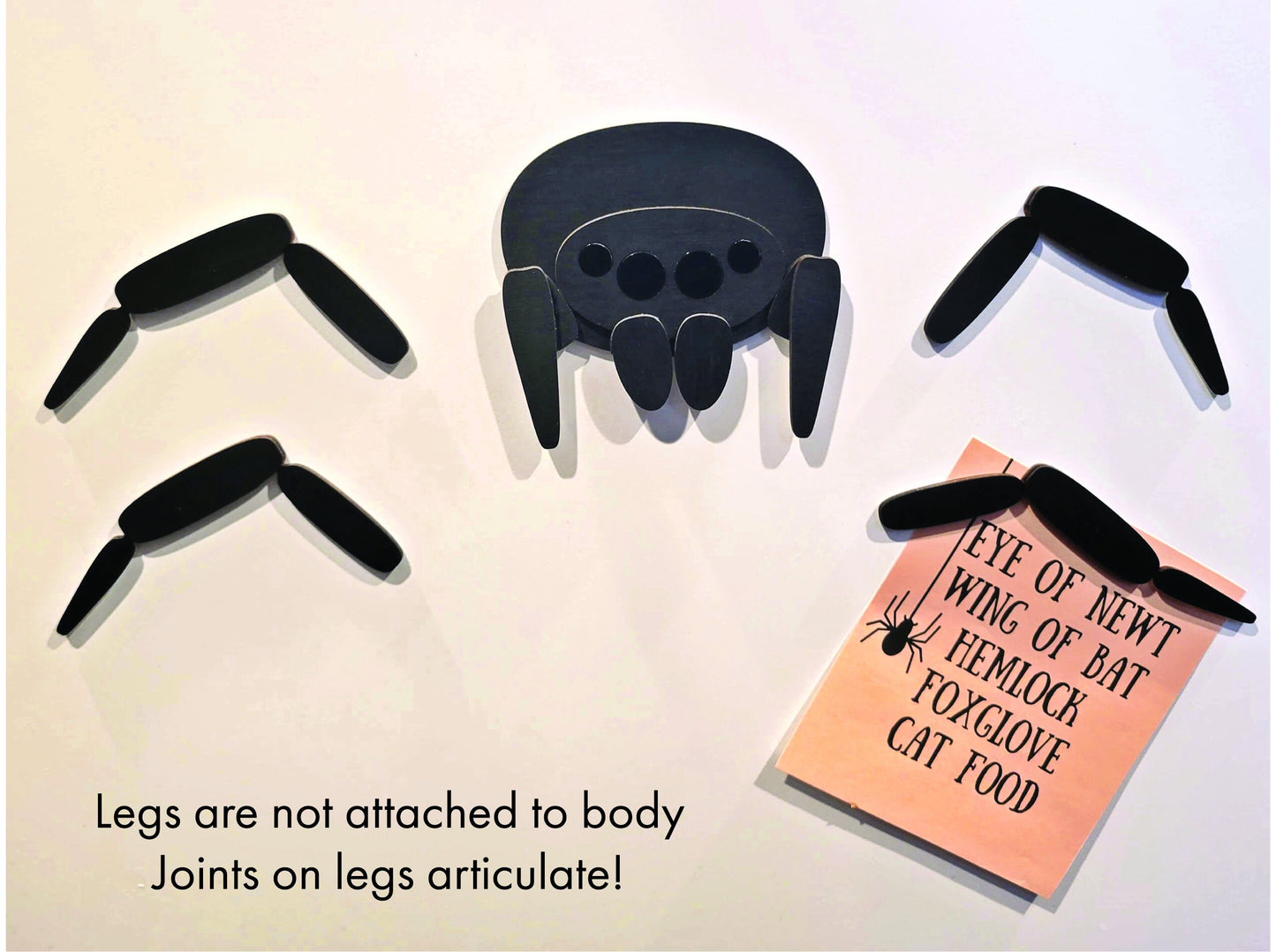 Laser-etched black wood spider magnet with bendable jointed legs, neodymium base, plus pink potion ingredient card—unique fridge decor.