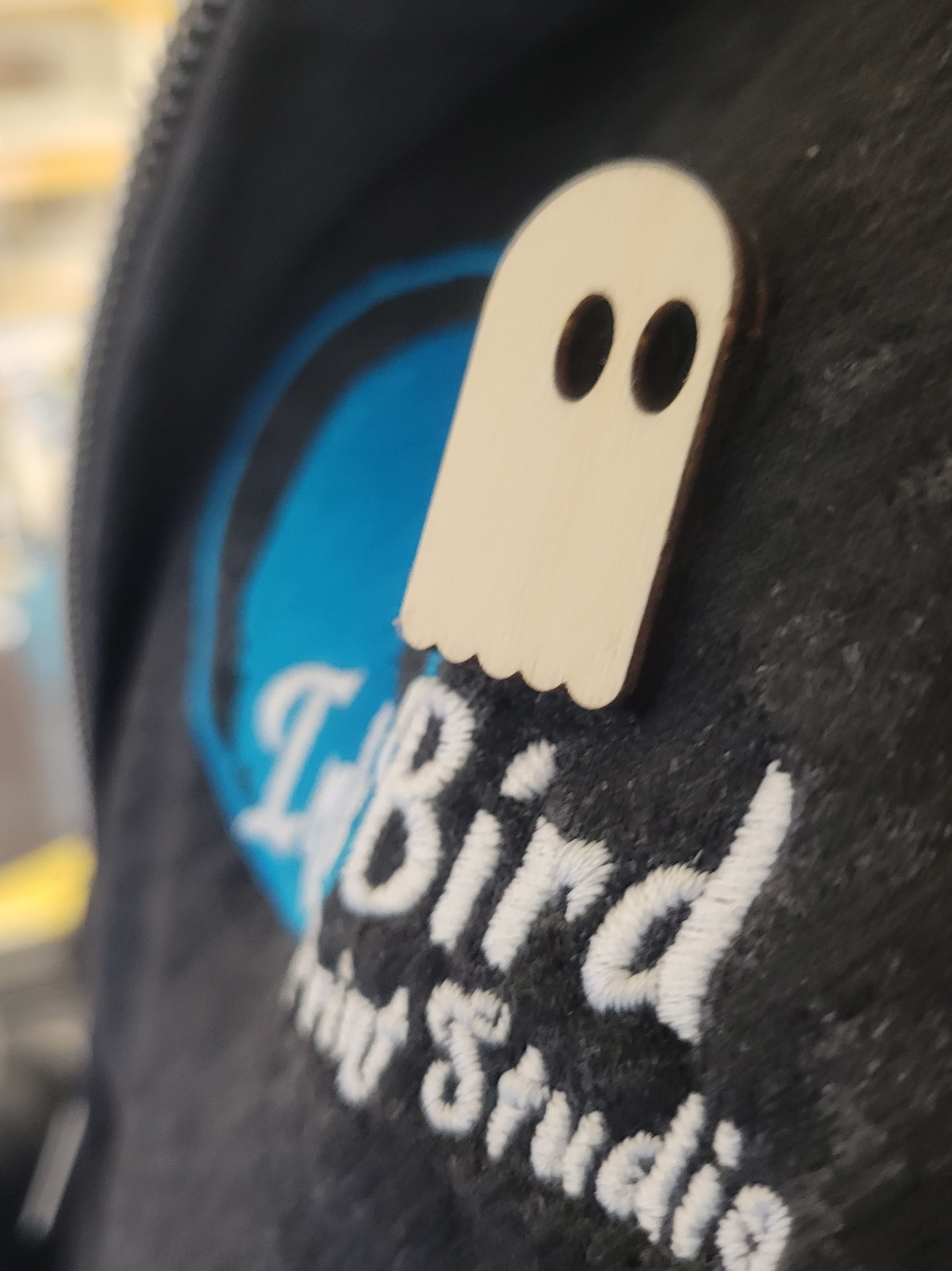 Birch wood ghost-shaped pin with black eyes, laser cut, on a hoodie with blue/white InkBird Print Studio embroidery.
