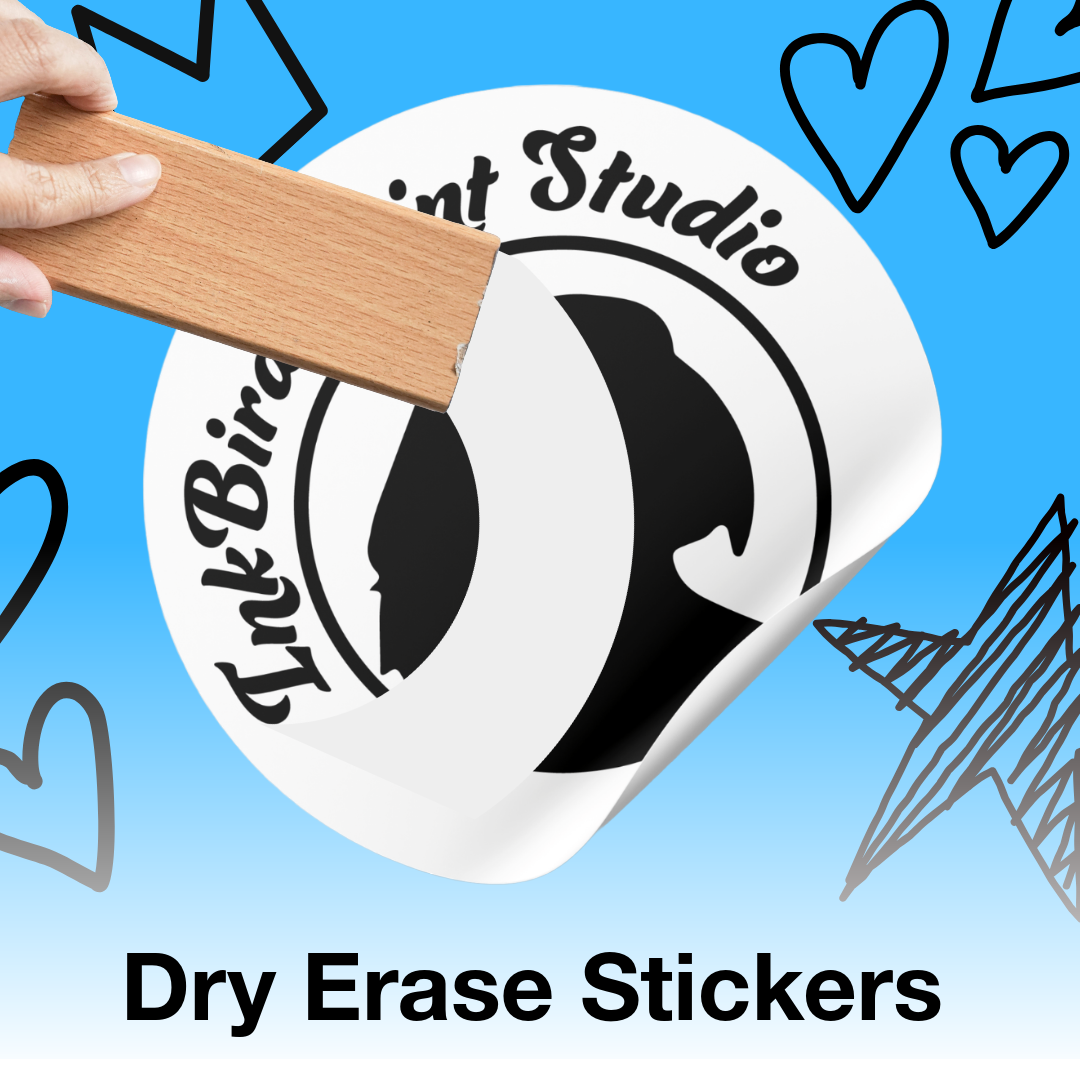A hand holds a wooden block against a white circular sticker that reads 'InkBird Print Studio' with a black bird silhouette. The sticker is shown on a bright blue background with doodled heart and line drawings, and the text 'Dry Erase Stickers' appears at the bottom.