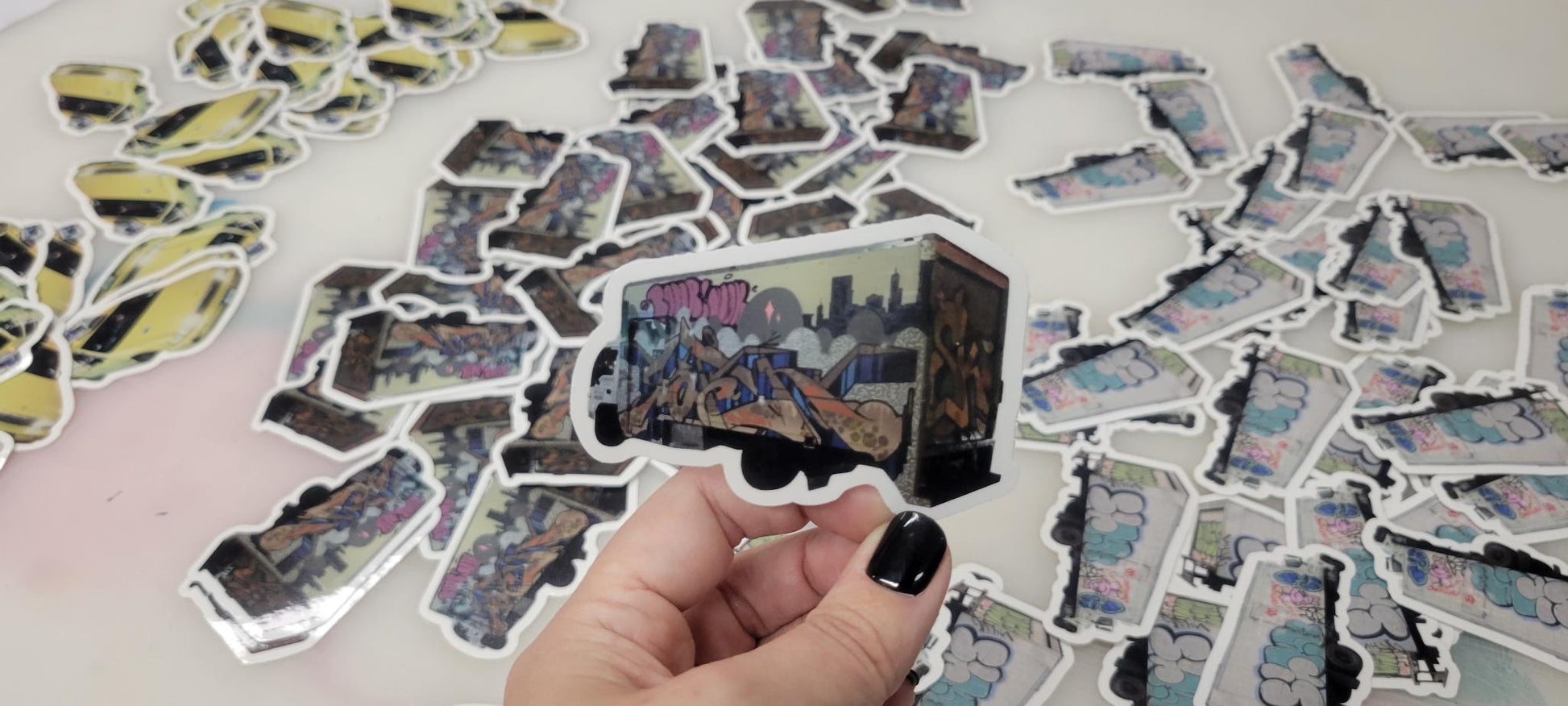 Die cut vinyl sticker of a graffiti truck by InkBird Print Studio, held by hand with black nails; custom stickers on white background.