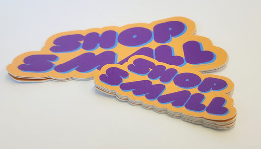 Stack of weatherproof vinyl Shop Small decals by InkBird Print Studio, bold purple text on orange, adhesive backing, outdoor safe.