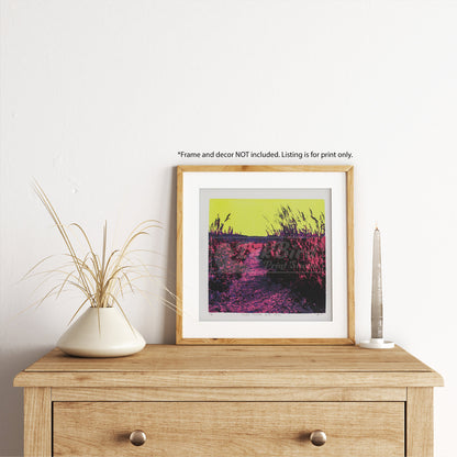 A wooden dresser showcases this hand-pulled, six-color screen print from InkBird Print Studio LLC, titled "Alien Picture Rock Trail" offers an alternate colorized view of Picture Rock Trail in Lyons, CO. The scene is framed by tall grasses and plants and is dominated by psychedelic colors: a bright yellow sky, deep pink path, and purple vegetation create an abstract and surreal landscape. Please note that text above the frame mentions it is not included in the listing.