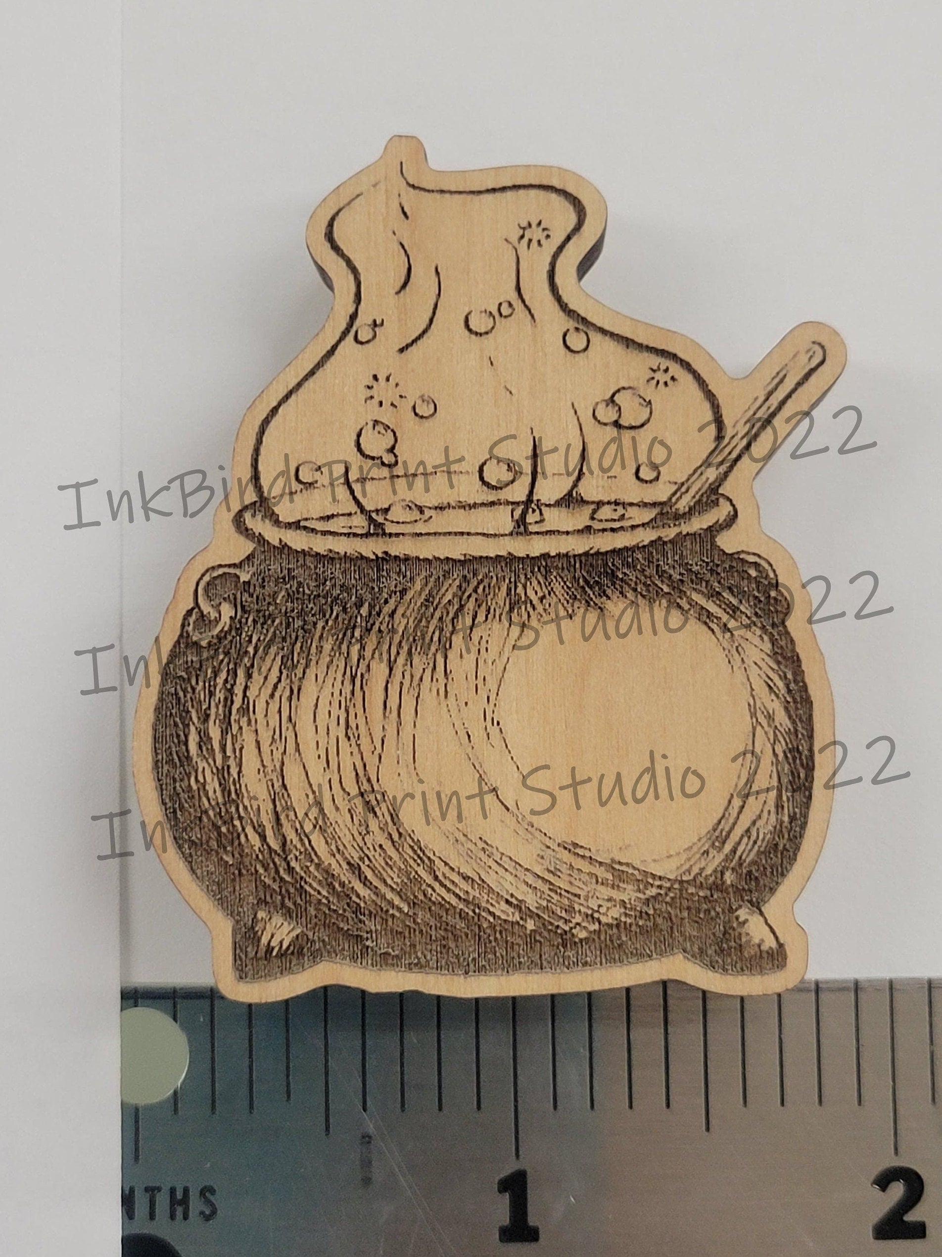 Laser-etched wood magnet shaped like a bubbling cauldron with spoon, natural brown finish, neodymium backing, approx 2 tall.